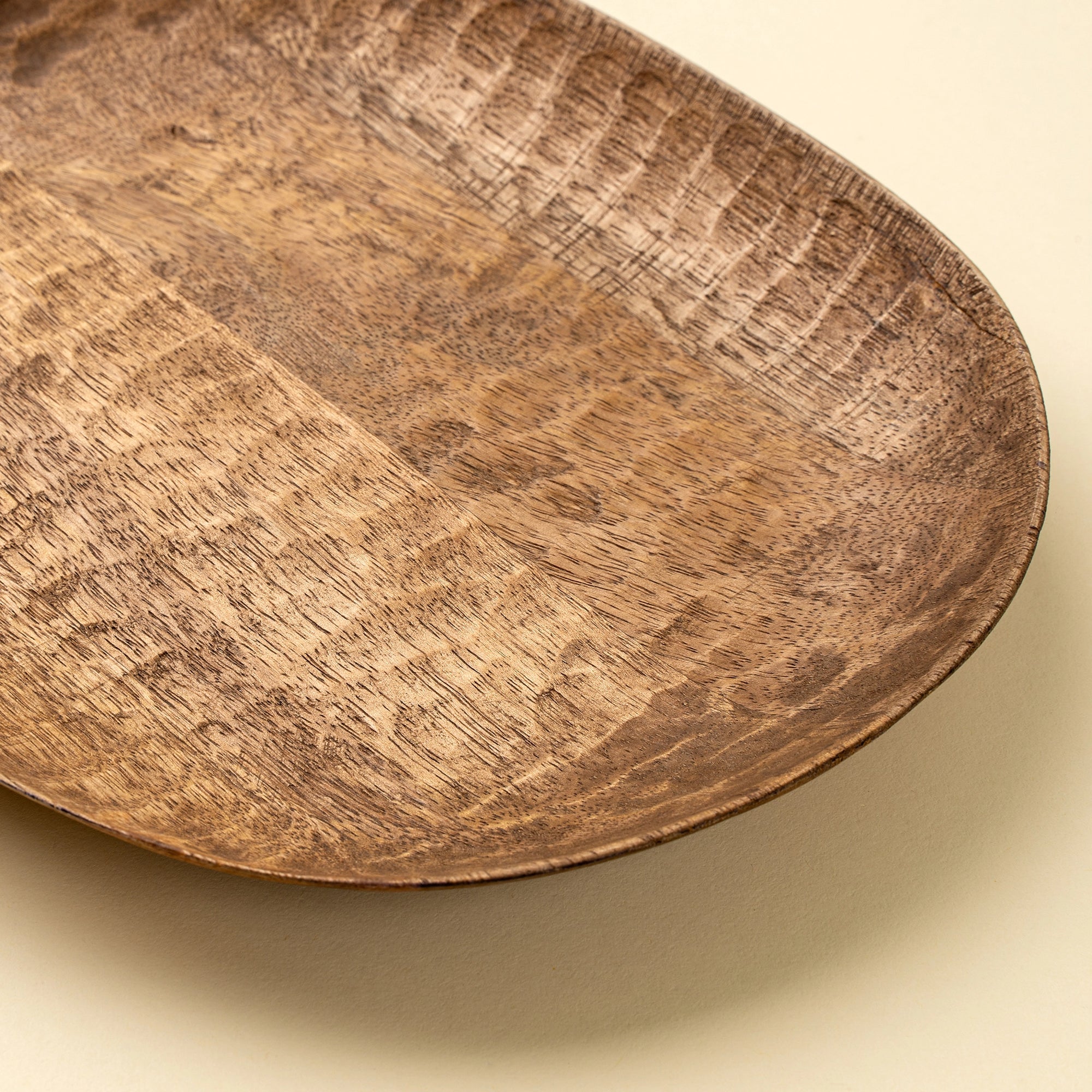 Hand-carved mango wood dish by Faire Terrain in natural finish, shown on a light beige background.