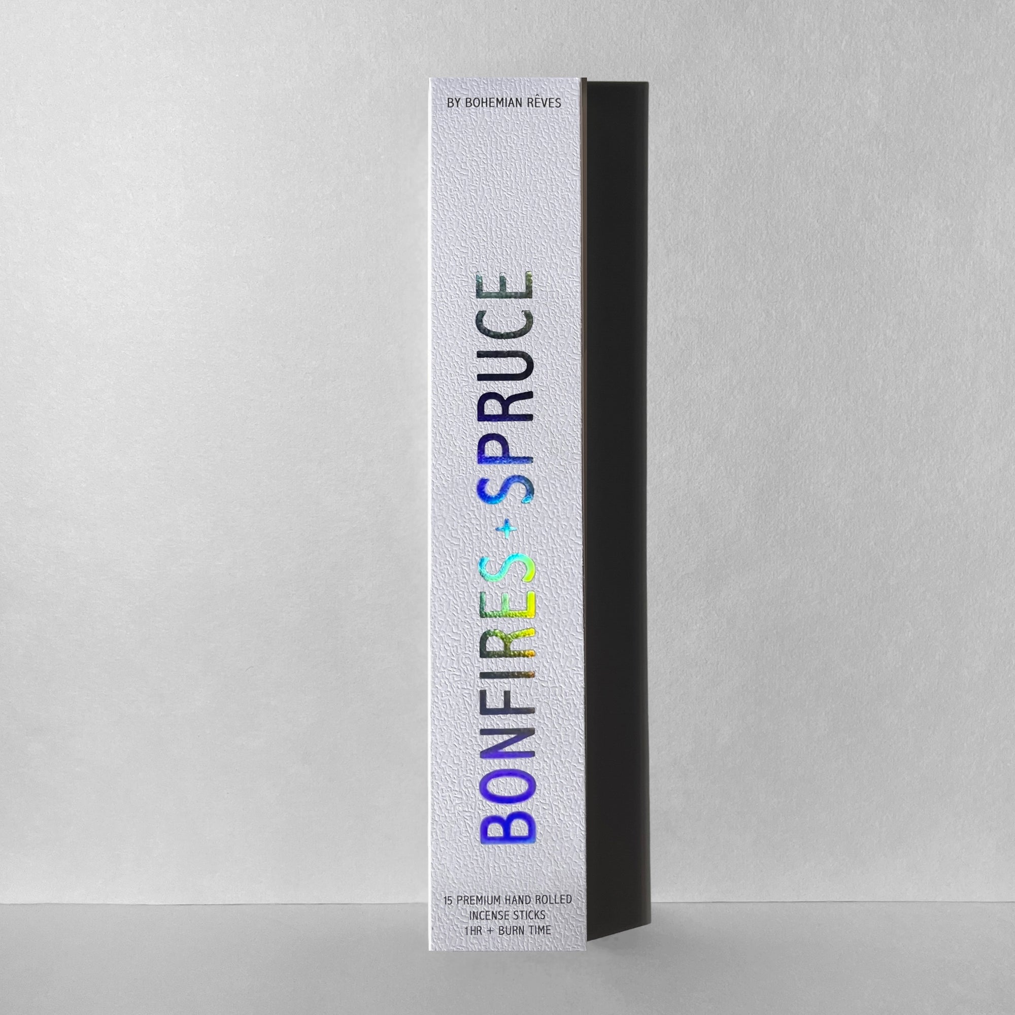 A white rectangular box of Faire Incense Sticks stands upright against a light gray background. "BONFIRES + SPRUCE" is in holographic text, with notes of Sandalwood Resin and "BY FAIRE" in smaller text at the top.
