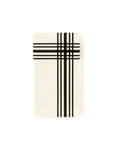 The MME Napkin by Faire features a white rectangular design with a plaid pattern of black intersecting lines in one corner, set against an otherwise plain white background.