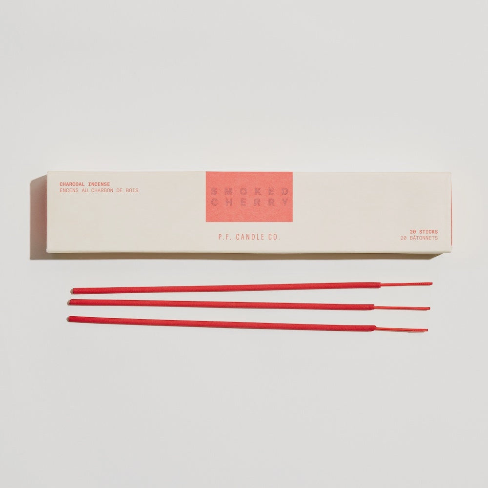 A box of Faire PFC Incense Sticks in "Smoked Cherry" sits on a white surface, capturing the rich Marasca cherry essence. Beside it, three red sticks lie horizontally, their sleek minimalist packaging embodying a chic HI-FI style with bold red text.