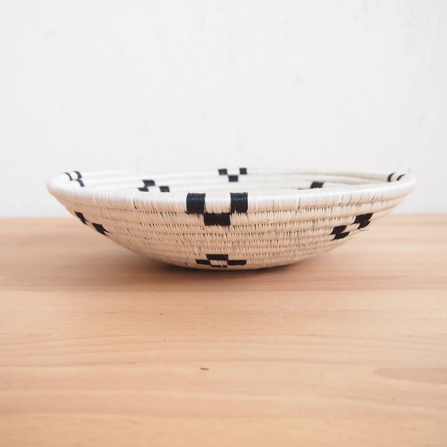 The Maraba Small Bowl by Amsha - Faire is a shallow, round sisal basket featuring a white base with black geometric patterns—ideal as wall art or a unique accent piece.