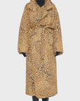 A person stands against a plain background wearing Norma Kamali's Classic Sleeping Bag Coat, showcasing its signature long, leopard-print design. The high collar and belt add flair to the ensemble, while black gloves and boots complete the look. Their neatly tied-back hair exudes both warmth and style.