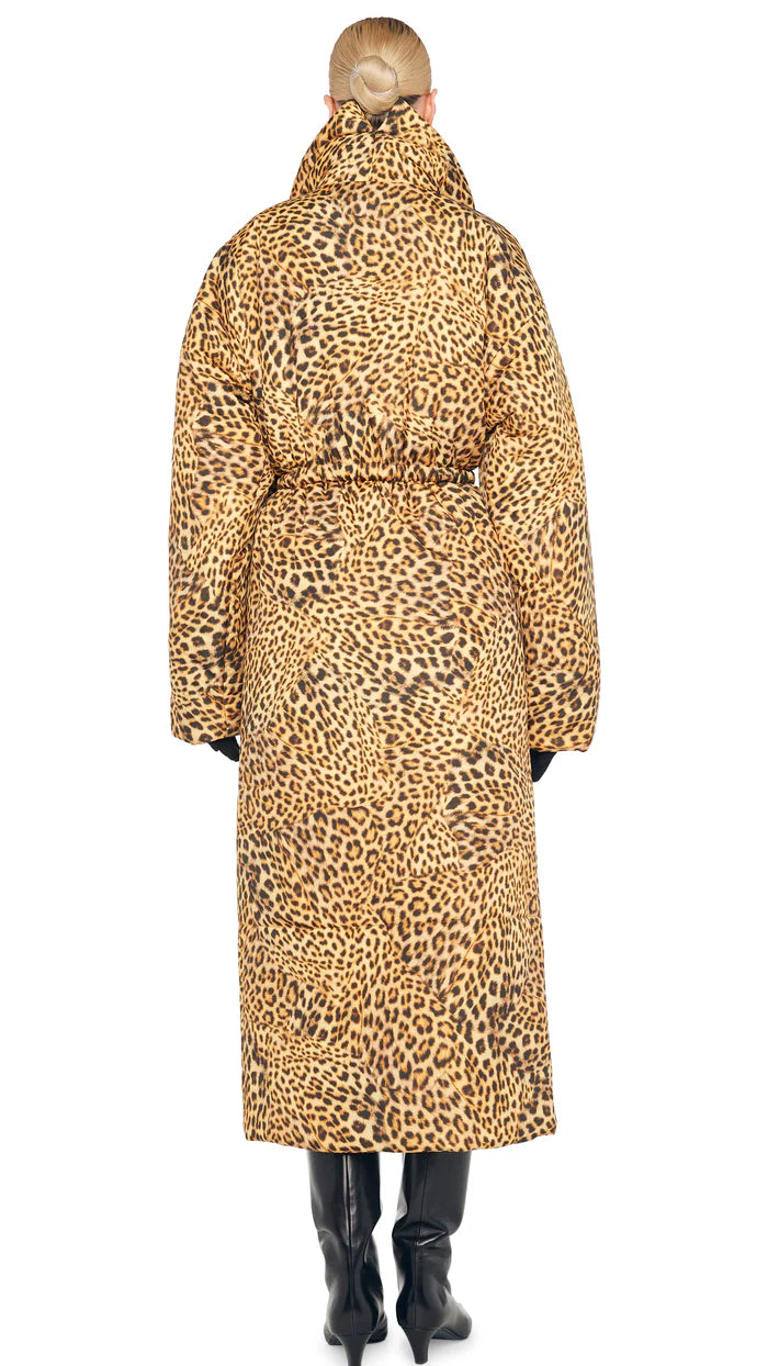 A person wearing the Classic Sleeping Bag Coat from Norma Kamali, featuring a long leopard print design reminiscent of the iconic sleeping bag coat style, stands facing away, highlighting its detailed pattern and oversized silhouette with black gloves and boots.