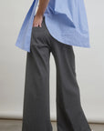 A person is wearing a wool blend blue striped shirt and Connor Wide Leg Pants from Aquarius Cocktail, standing against a plain background with one hand on their hip. Only part of their body is visible. They are also wearing white shoes with red stripes, adding a unique touch to this small batch ensemble.