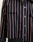 Close-up of someone wearing the Aquarius Cocktail "Yes Sir" cropped jacket in navy blue with red and white stripes over a black polka dot shirt. The jacket offers buttons, pocket flaps, and a relaxed fit, accessorized with a pearl necklace for a stylish look.