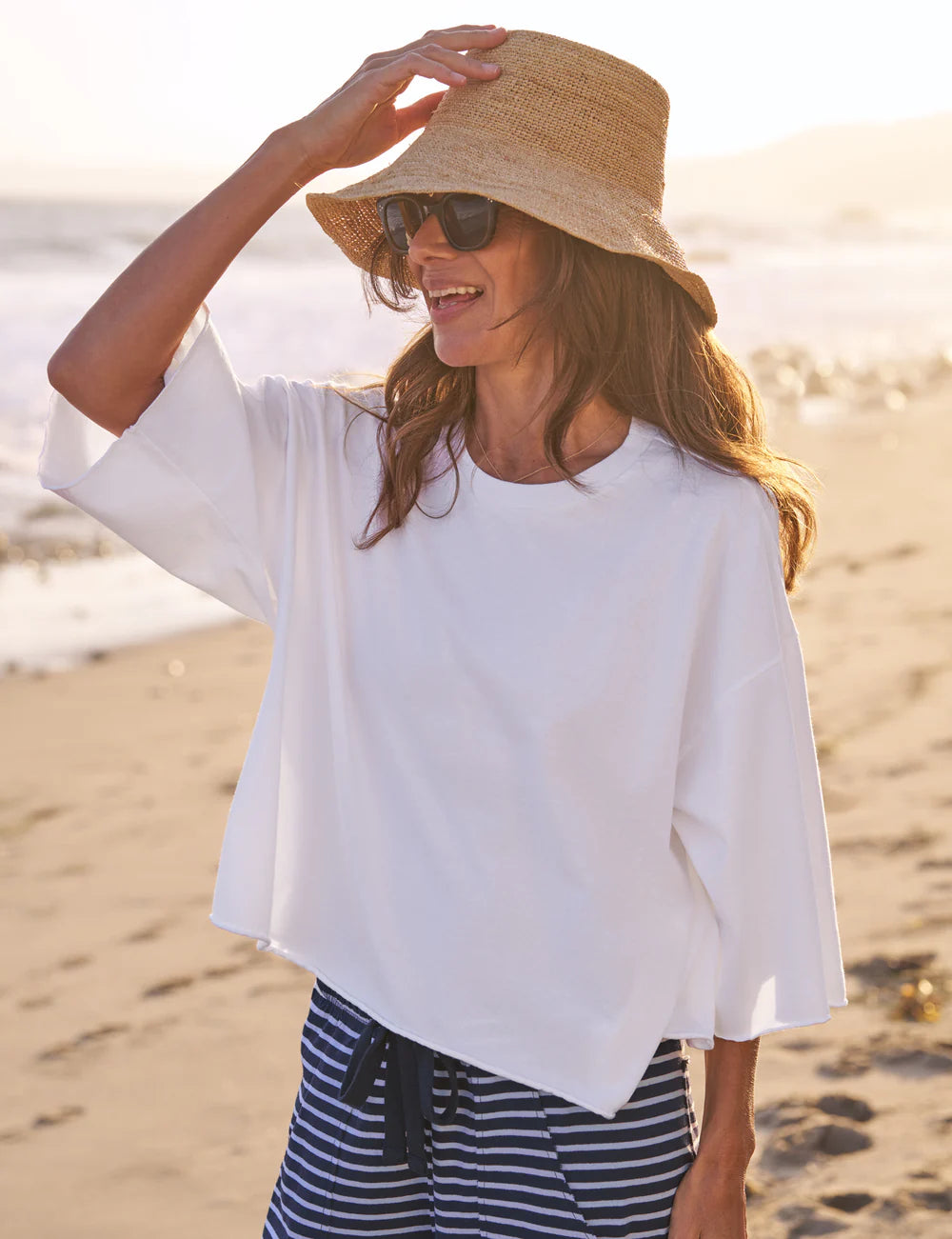 Frank &amp; Eileen Presley Oversized Tee styled with striped pants and sunhat on a sandy beach at sunset.