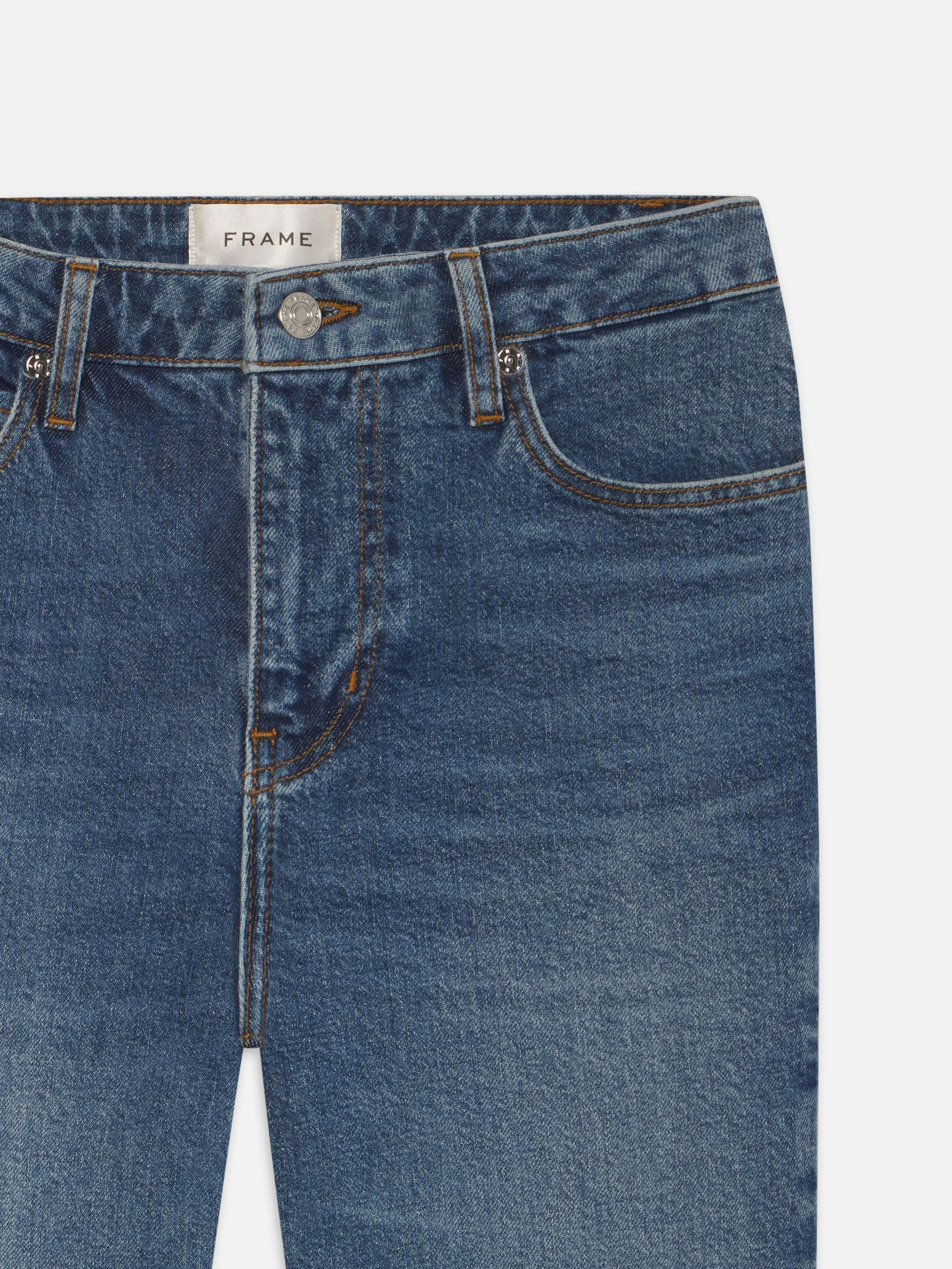 Close-up of FRAME's The Ruler Crop jeans in medium-blue denim, featuring front pockets, belt loops, button closure, and an inner waistband label—crafted in a slim-straight leg style.