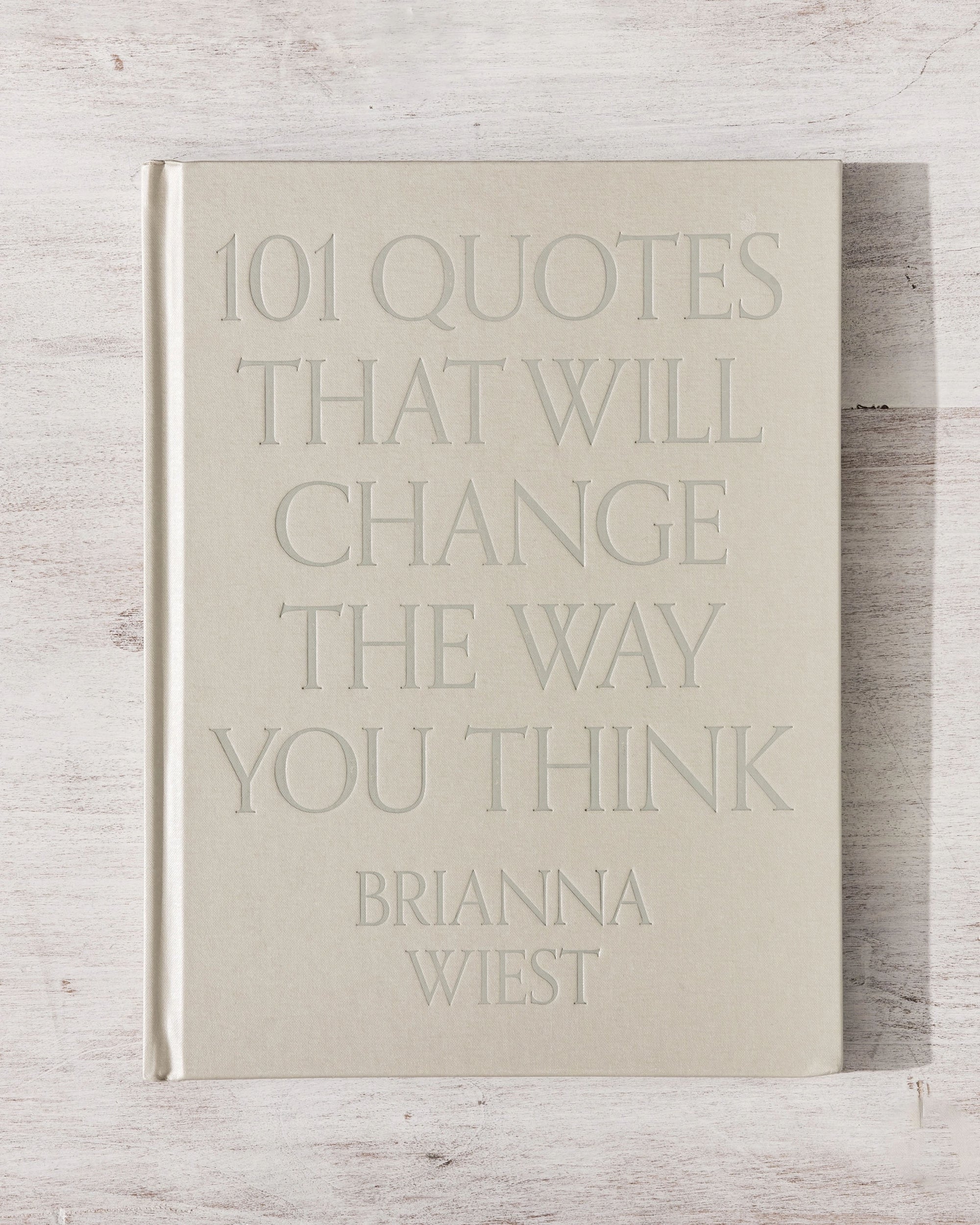 A beige hardcover copy of "101 Quotes That Will Change the Way You Think" by Faire rests on a light wooden surface.