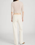 A person with long brown hair, seen from behind, wears a light pink textured knit top and FRAME’s The Saturday Jean—high-waisted, off-white 100% cotton wide-leg denim—paired with beige shoes against a plain light background.