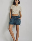 Denimist indigo UTILITY SHORT styled with a cropped beige polo and white sneakers against a bright background.