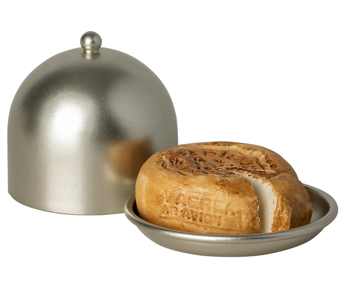 A round loaf of bread with a missing slice sits on a small metal plate beside a matching dome lid from Maileg Furniture by Maileg—ideal as dollhouse decor for your Maileg Mouse.