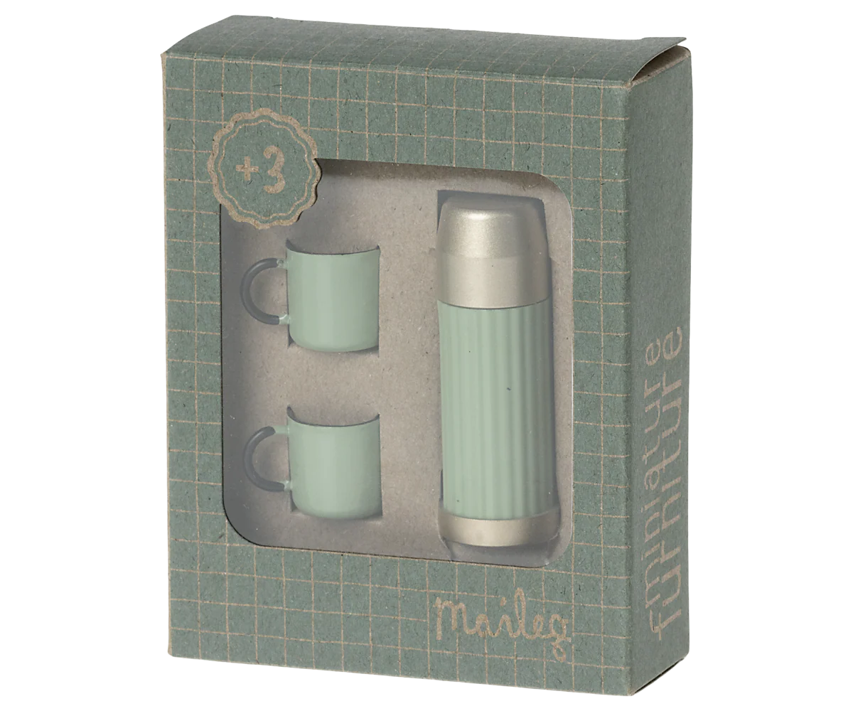 The Maileg Thermos & Cups set features a green and silver thermos and two green mugs for hiker mice, packaged in a windowed box with a grid pattern and the Maileg brand name on the front.