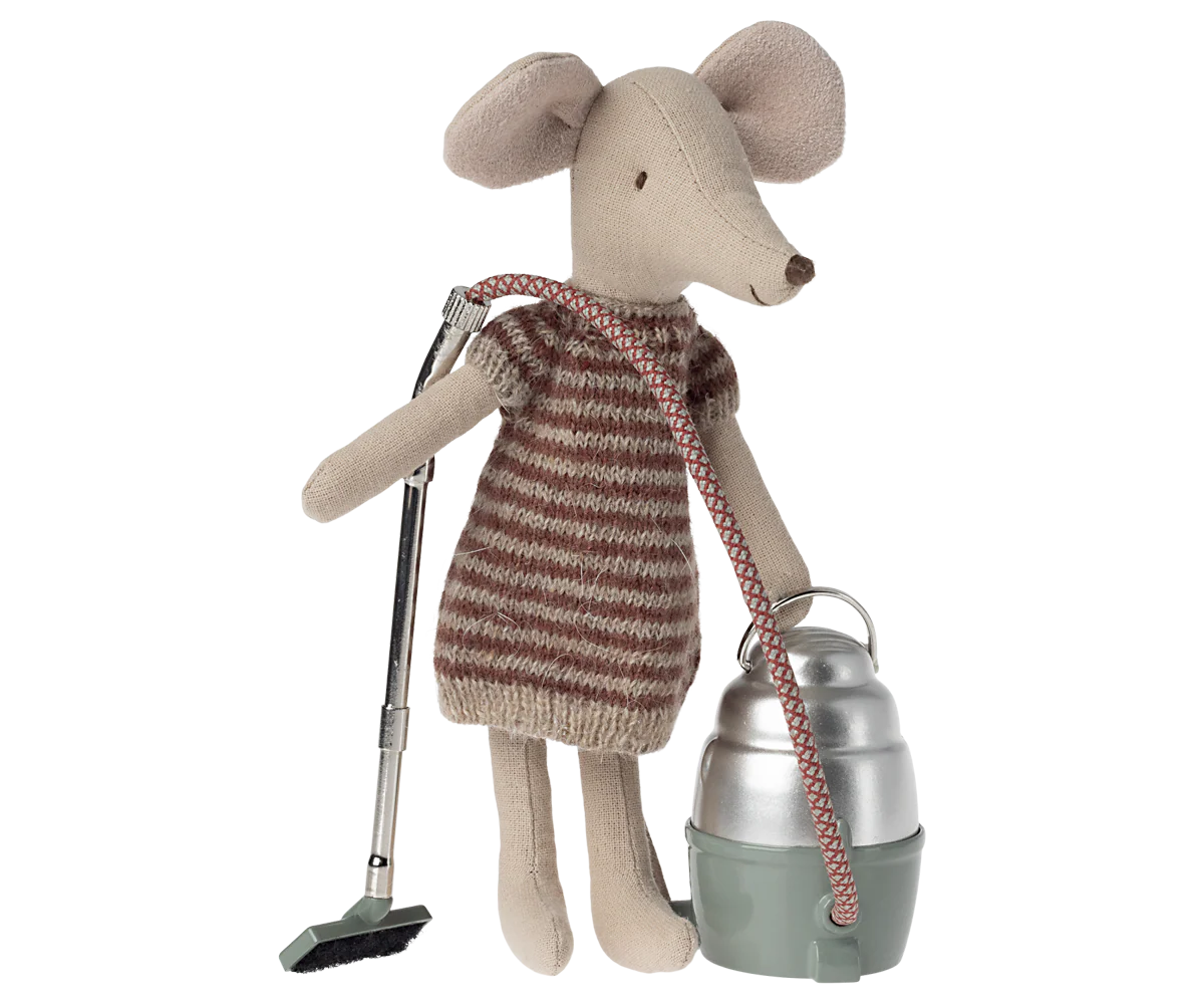 A Maileg stuffed mouse in a striped dress holds the hose of a Maileg Vacuum Cleaner toy, ready to clean. The soft mouse features fabric ears and a stitched nose, with the vacuum cleaner standing beside it.