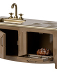 The Maileg Kitchen by Maileg is a miniature gold and bronze dollhouse set featuring a sink, stove burners, and two open oven compartments, one with a small cooked roast inside.