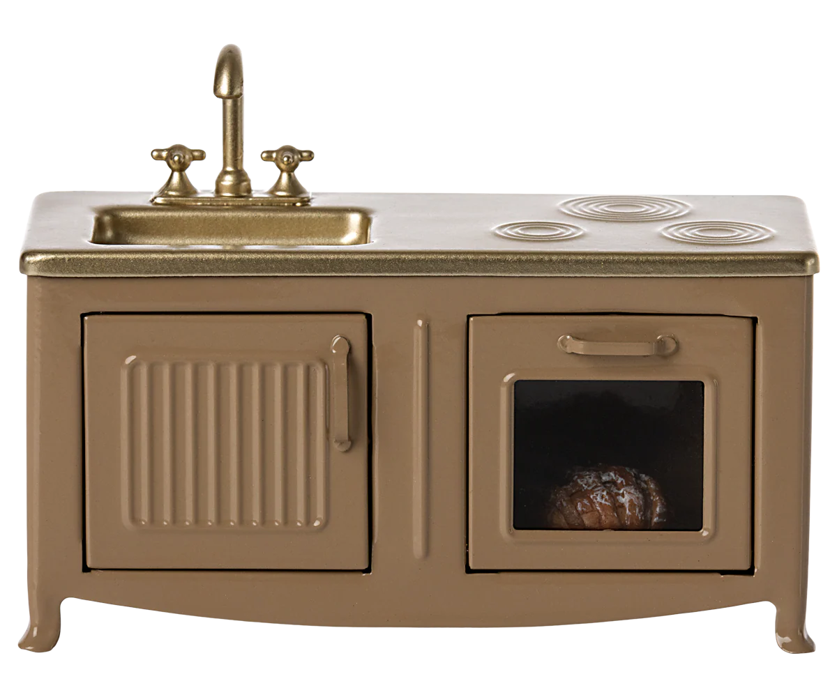 The Maileg Furniture brown miniature kitchen set by Maileg features a gold sink and faucet, two burners, a cabinet with a vertical handle, and an oven with a window showing food—perfect for any Maileg Mouse dollhouse.