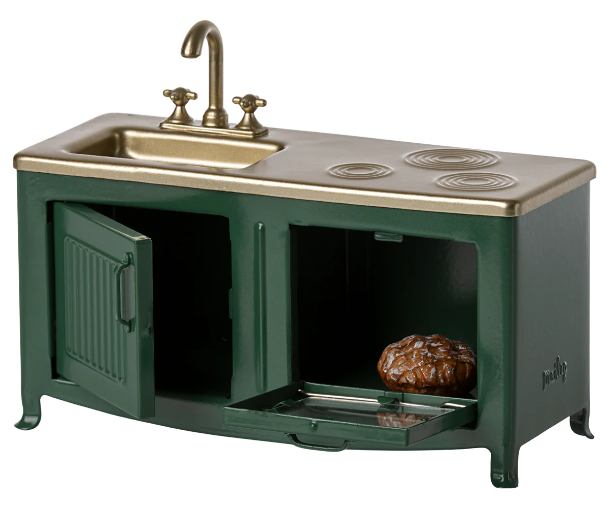 The Maileg Furniture miniature green and gold kitchen set by Maileg is ideal for dollhouses, featuring a sink, faucet, burners, and oven with opening doors—one reveals a tiny pie inside.