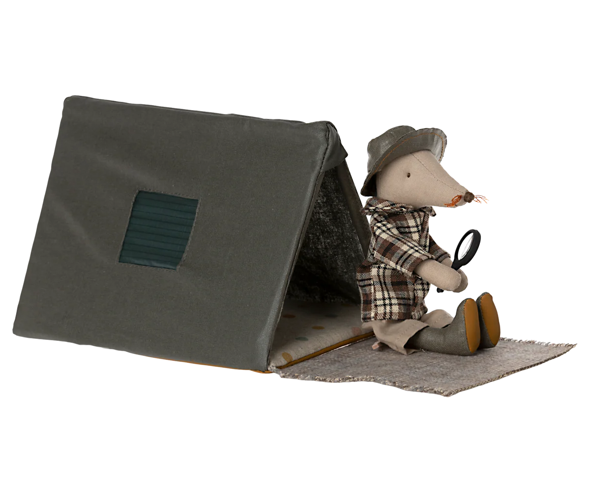 A Maileg toy mouse sits at the entrance of the Maileg Happy Camper Single Tent, dressed in plaid clothes and a hat, holding a magnifying glass. The cozy gray tent features a square window and front mat for imaginative play.