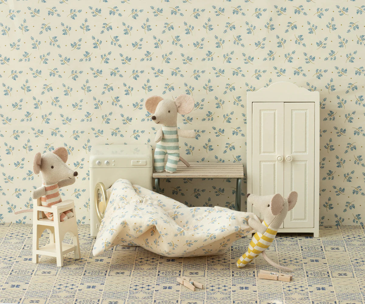 Three toy mice in striped outfits play in a vintage-style laundry room with floral wallpaper, tiled floor, scattered laundry, and Maileg accessories like the Maileg High Chair, washing machine, bench, and wardrobe.