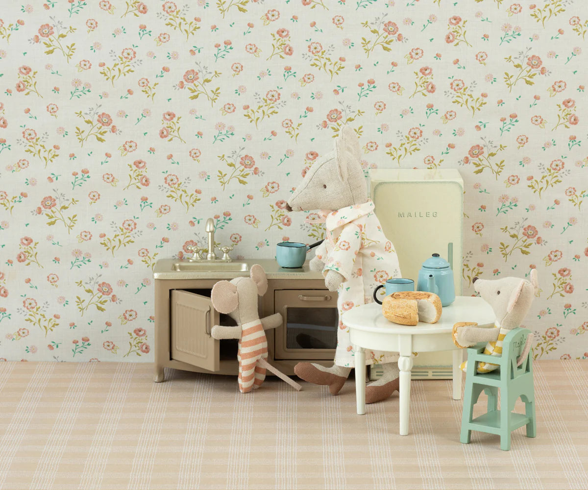 Three Maileg toy mice in a vintage-style kitchen: one stands at the sink, one in striped pajamas reaches for the counter, and another sits at a table set with bread, a blue teapot, dollhouse furniture, and the adorable Maileg High Chair.