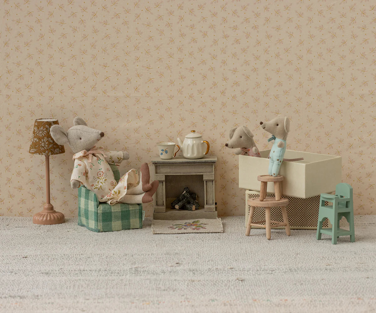 Three toy mice relax in a Maileg home, complete with the Maileg Fireplace, green chair, blue stool, teapot, lamp, and tiny furniture set against floral wallpaper for a charming vintage look.