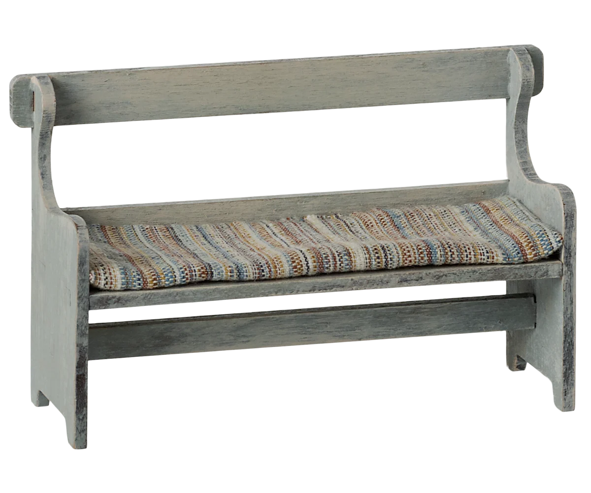 The Maileg Bench by Maileg features a cushioned seat with striped, multicolored fabric, backrest and arms. Its weathered grayish wood finish adds vintage charm to this classic small bench.