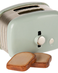 A cute, light green two-slot toaster with a round knob and two slices of toast sits in front—perfect Maileg Furniture by Maileg for dollhouses or miniature toy displays.