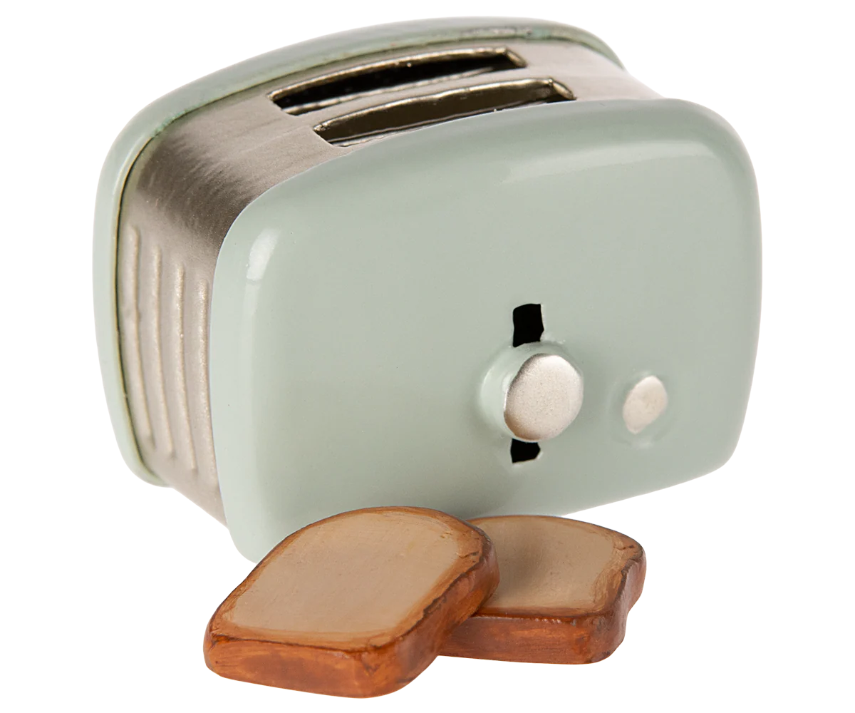 The Maileg Toaster by Maileg is a small, light green metal toaster with two slots and a knob, shown beside slices of toasted bread—miniature accessories ideal for a whimsical Mouse Hole Farmhouse scene.