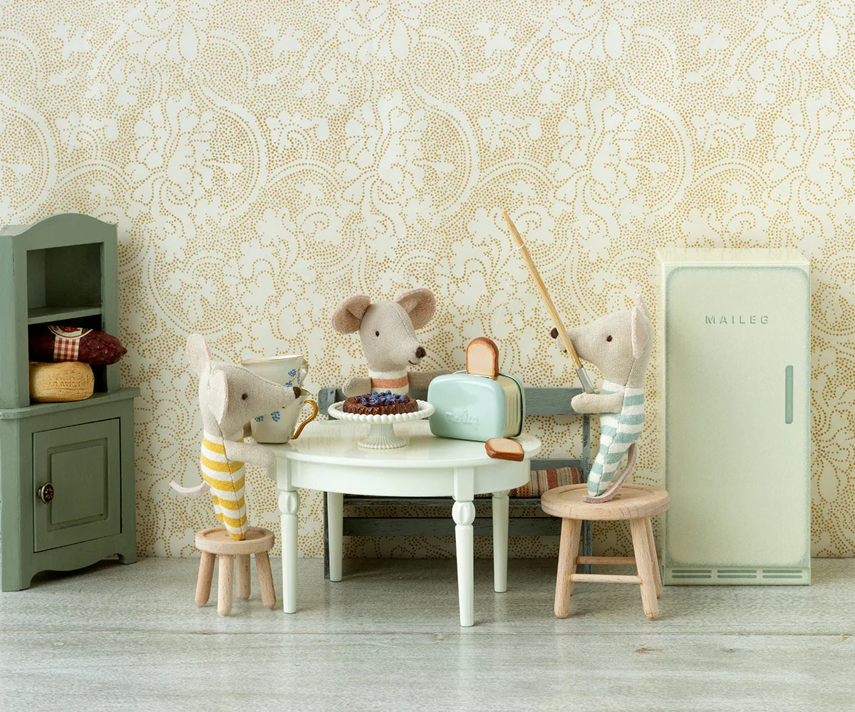 Three toy mice gather around a table with a cake in the vintage-style Mouse Hole Farmhouse kitchen, surrounded by pastel furniture, patterned wallpaper, tiny kitchen accessories, and the Maileg Toaster by Maileg with toasted bread.