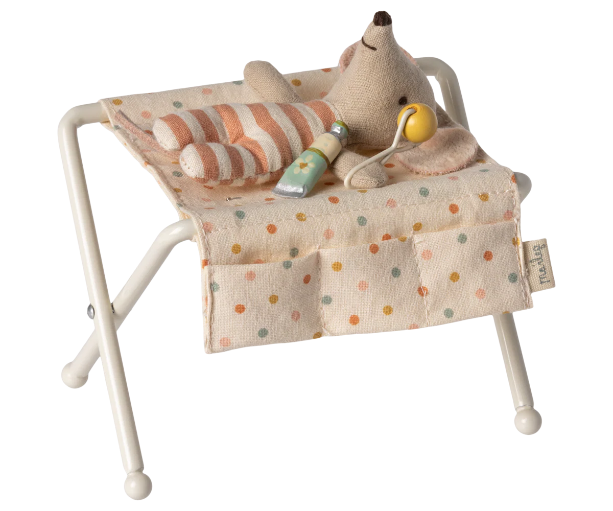A Maileg Nursery Table by Maileg features a small plush baby mouse in striped pajamas, lounging with a yellow pacifier and green bottle, surrounded by charming baby accessories.