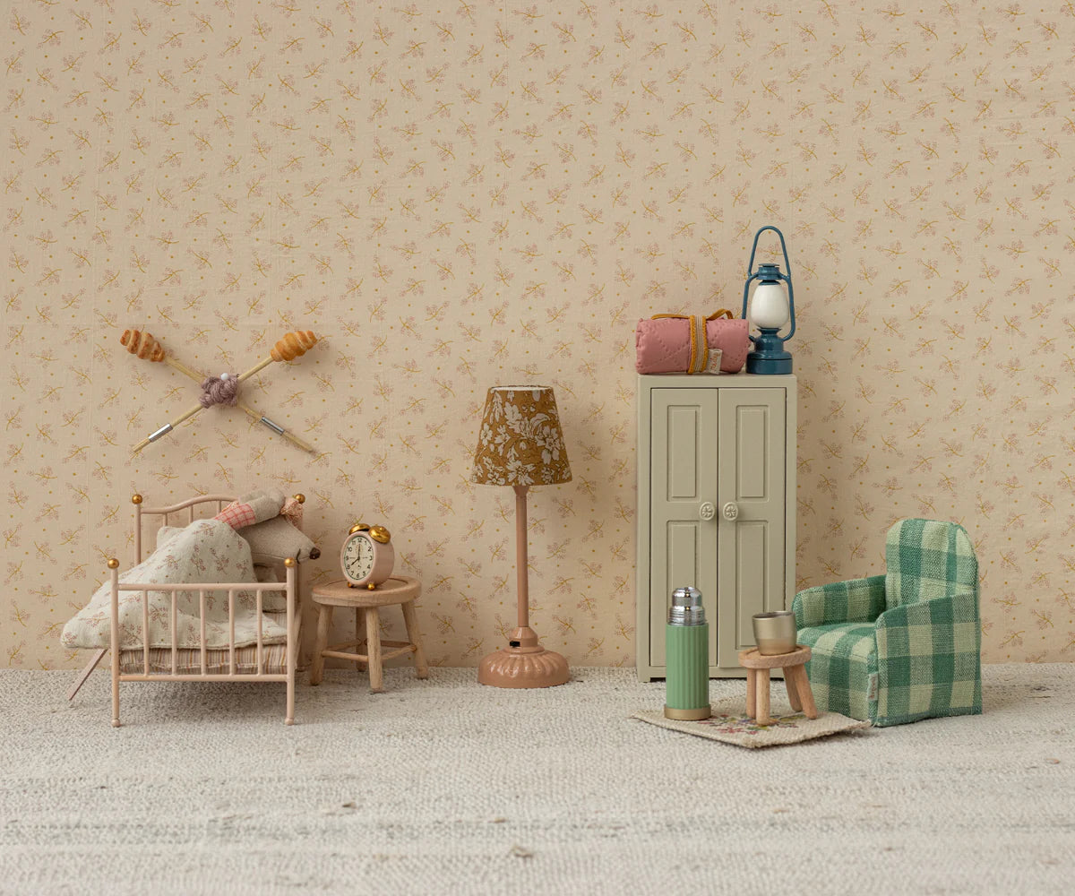 A miniature dollhouse room features a small bed, pillows, blanket, vintage alarm clock, lamp, green plaid armchair, tiny table with thermos and cup, cabinet with bags, and the Maileg Vintage Lantern by Maileg against floral wallpaper.