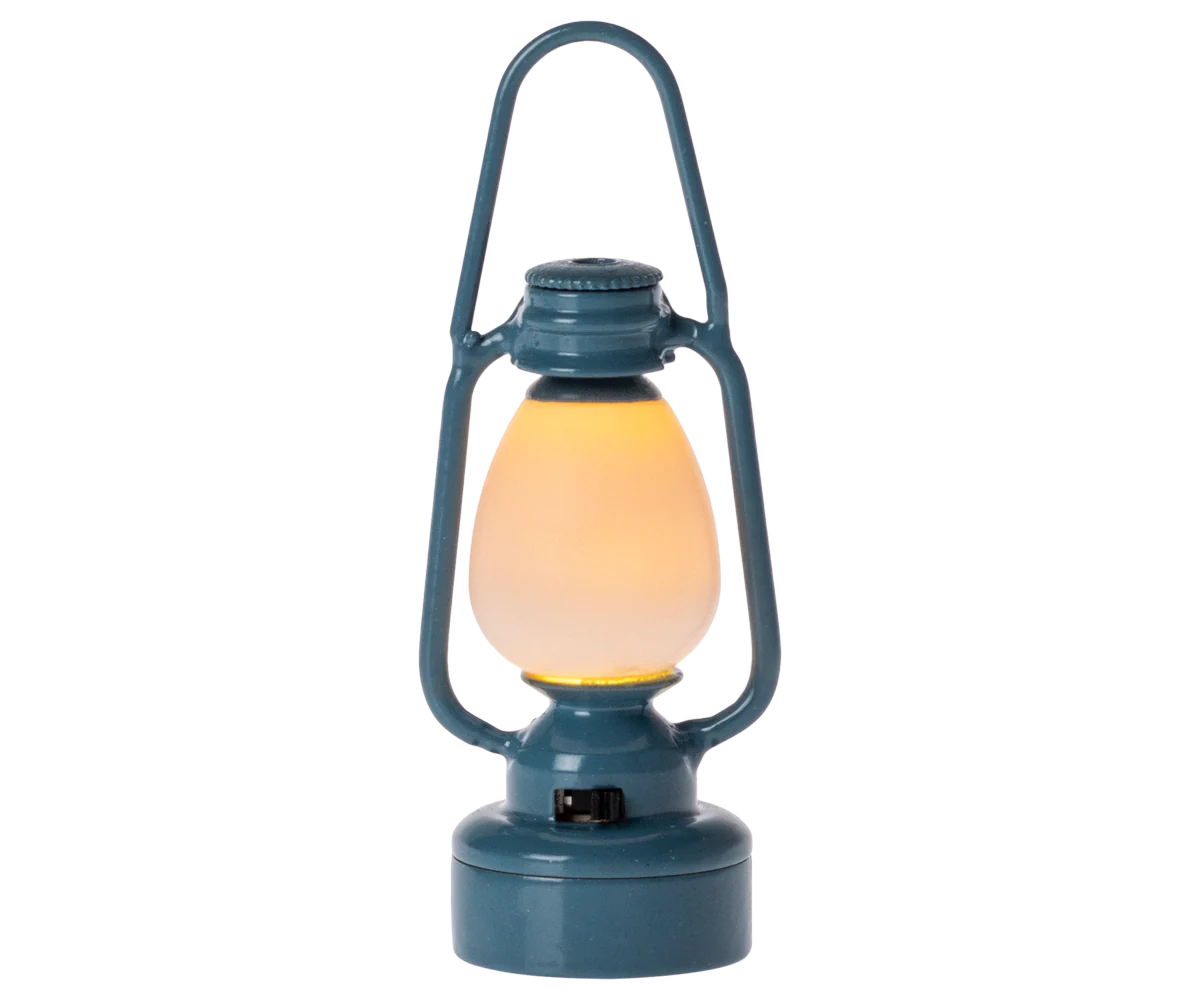 The Maileg Vintage Lantern by Maileg is a blue, vintage-inspired miniature lantern with a glowing yellow light inside, powered by a coin cell battery, displayed against a plain white background.