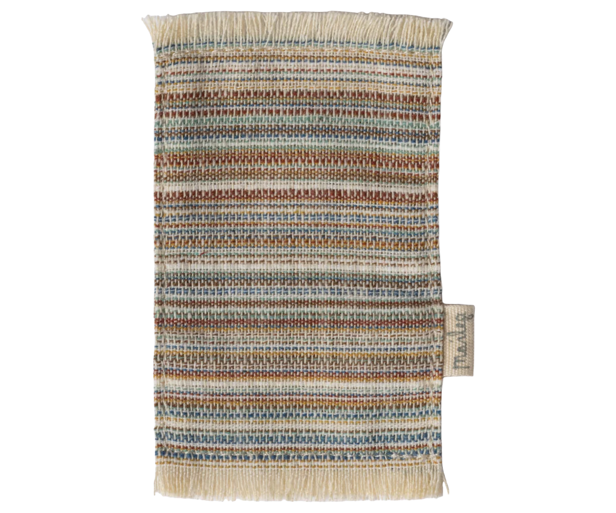 The Maileg Rug by Maileg is a rectangular woven swatch with brown, blue, green, and beige horizontal stripes, fringed edges, and a side tag—perfect as a doll house doormat or for decorating small interior spaces.