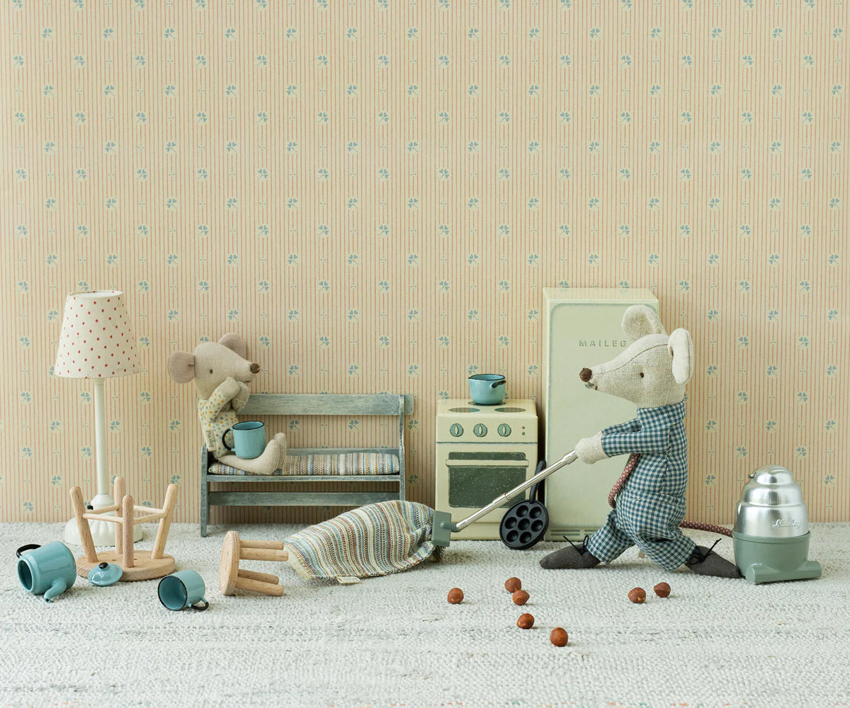 Two toy mice in a miniature kitchen scene: one sips from a cup on a bench, while the other cooks at the stove. Dollhouse fans will love the detailed Maileg interior items, including the cozy Maileg Rug that completes this playful setup.