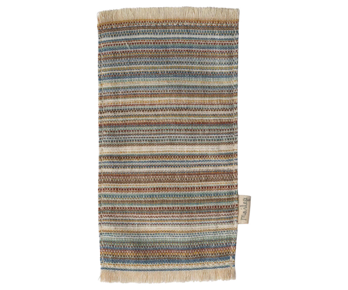 The Maileg Furniture is a cute rectangular woven rug by Maileg with blue, brown, beige, and tan stripes, fringed edges, and a fabric label—perfect as dollhouse decor.