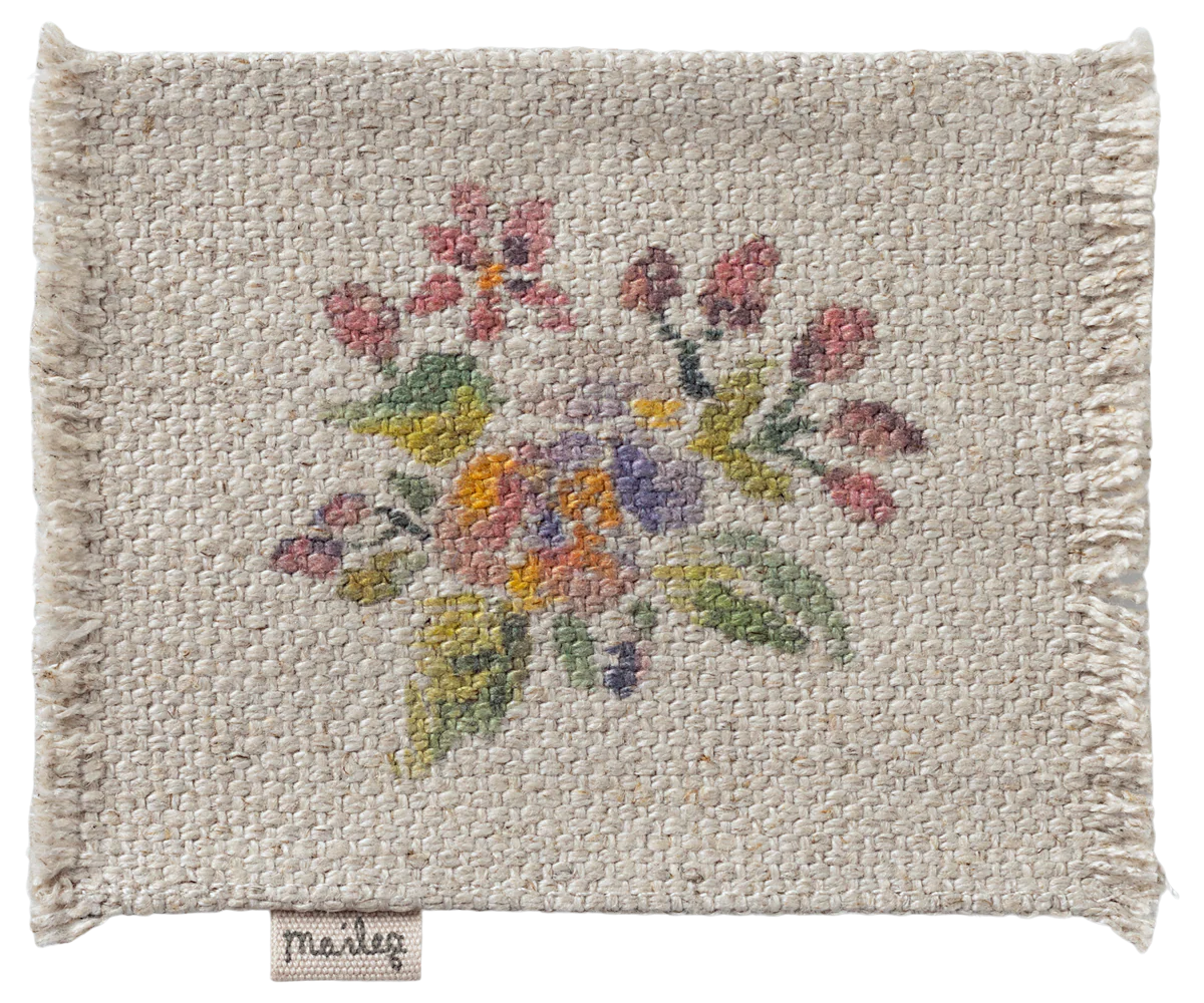 A square, textured Maileg Furniture piece by Maileg features frayed edges and a charming cross-stitched floral design in pink, yellow, purple, and green—ideal for dollhouse decor. A “Marley” label is stitched to the bottom edge.