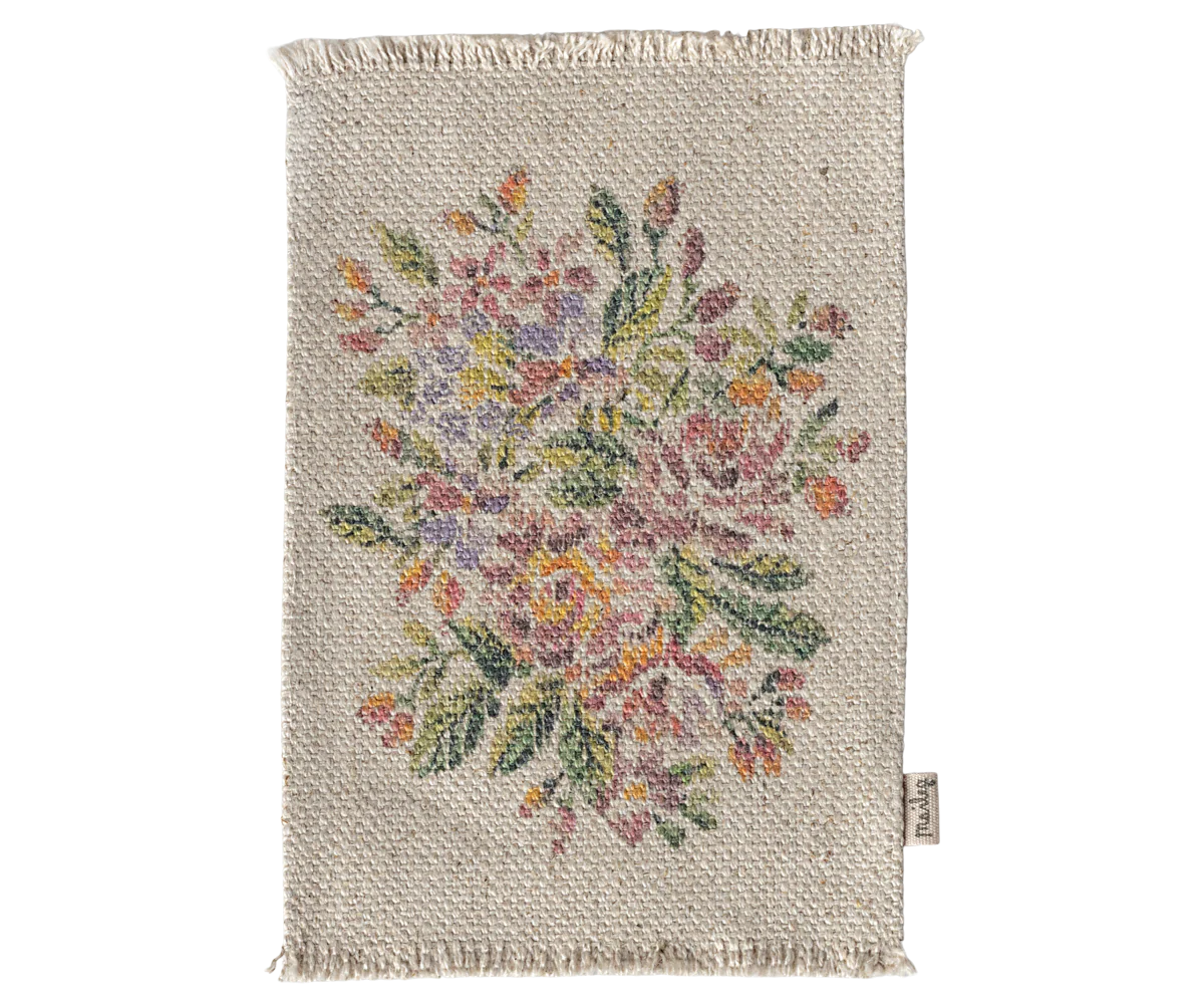 The Maileg Rug by Maileg is a rectangular woven mat with fringed edges and a vibrant floral pattern in pink, yellow, orange, and green on beige. It’s perfect as a doormat or for dollhouses and includes a small fabric tag on one side.