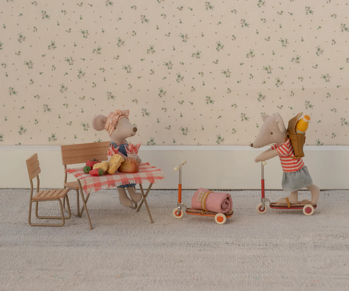 Two Maileg mice in a cozy scene: one wears a headscarf at the table with food, the other in a striped shirt and backpack rides the Maileg Kick Board. Both are surrounded by charming miniature furniture and wooden details.