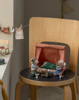 Three Maileg toy mice play: one lounges at a picnic table by the window, while two gather near the Maileg Happy Camper Mouse Tent on a wooden chair. Tiny clothes hanging on a string complete their cozy outdoor scene.