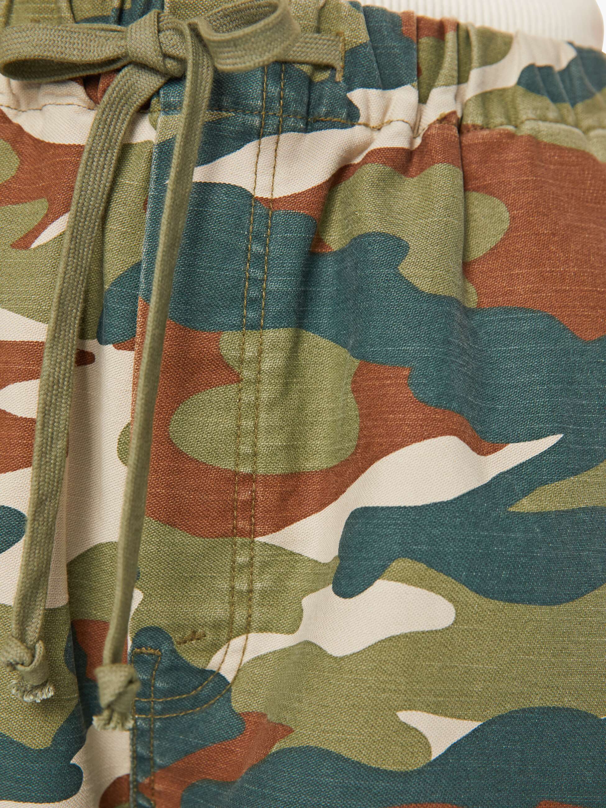 Close-up of The Drawn Half-Pipe Ankle by Mother, featuring 100% cotton camouflage fabric with green drawstrings. Shows high-waisted waistband, stitching detail, and shades of green, brown, and beige.
