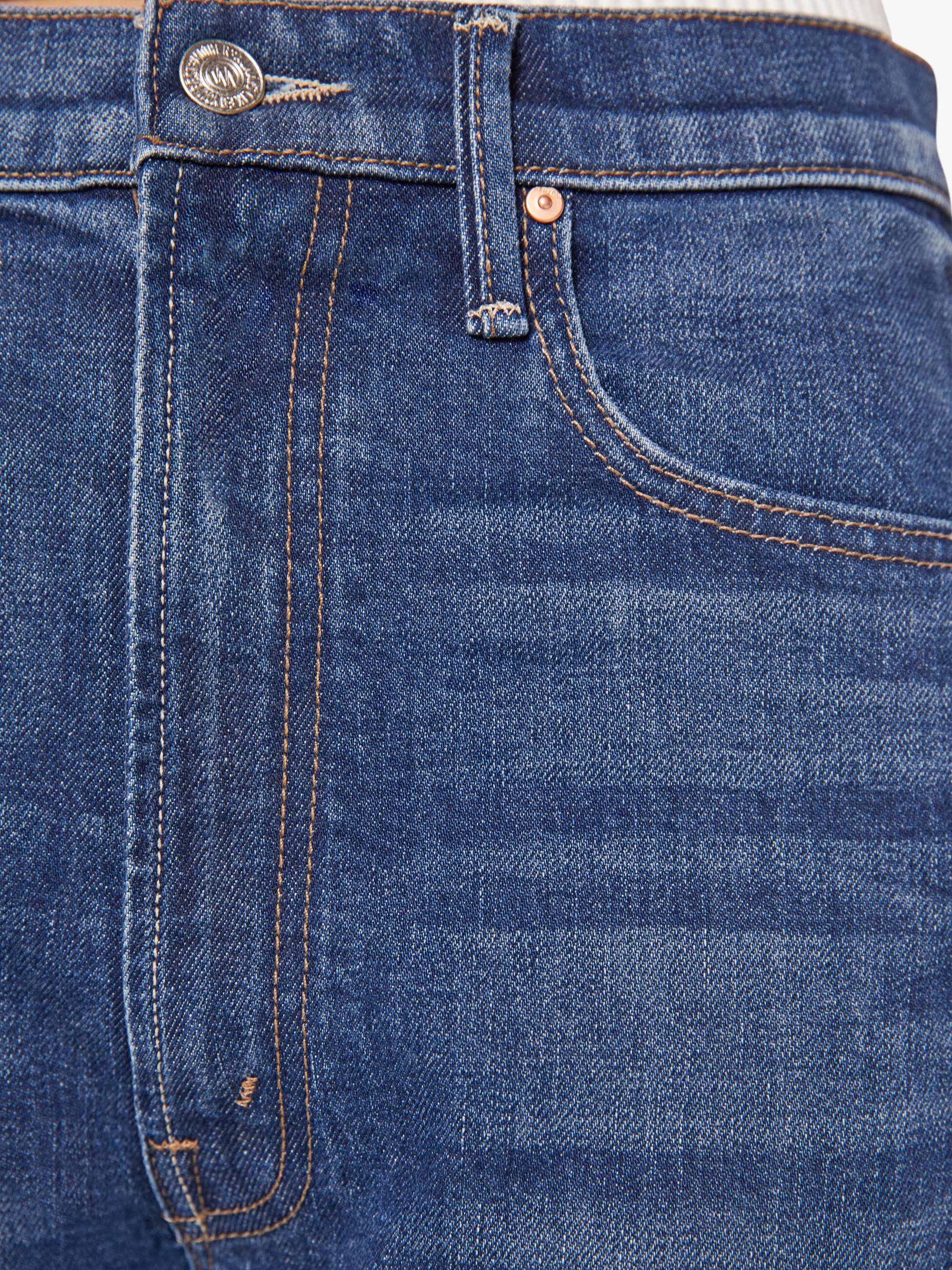 Close-up of The Half-Pipe Ankle Cuff Fray jeans by Mother, featuring a front pocket, waistband, belt loop, metal button, copper rivet, orange stitching, and textured superior denim fabric in dark blue.