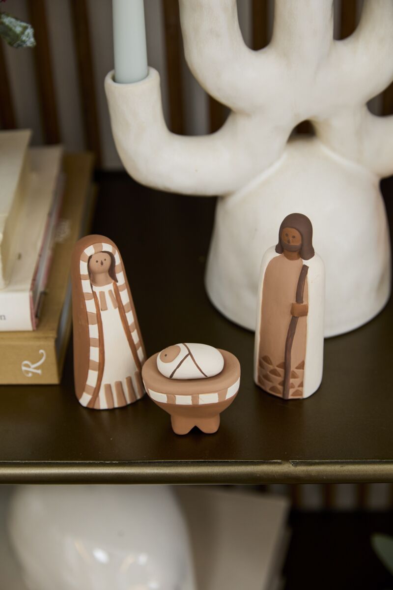 The Accent Decor Pintura Nativity is a handmade ceramic set with Mary, Joseph, and baby Jesus in a manger—perfect as Christmas decor for your home, displayed on a shelf with books and a white candleholder.