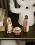 The Accent Decor Pintura Nativity is a handmade ceramic set with Mary, Joseph, and baby Jesus in a manger—perfect as Christmas decor for your home, displayed on a shelf with books and a white candleholder.
