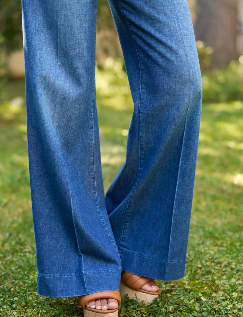 A person wearing the NYC Trouser by Frank &amp; Eileen and tan open-toe sandals stands on grass with blurred greenery in the background.