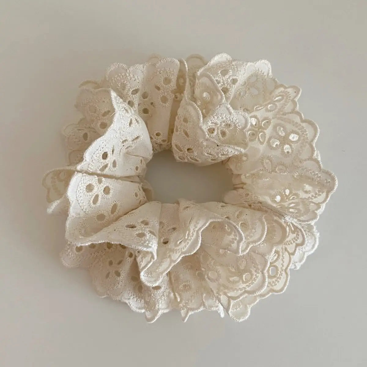 Faire Hair Scrunchies: Cream-colored lace with delicate floral cut-outs, styled in a circular shape on a plain light background—a charming pick for lovers of elegant hair accessories.