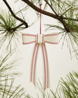 The Candace Ornament 5x9.5" by Accent Decor is a metal bow with red stripes, hanging among pine needles as a festive Christmas tree decoration against a light background.
