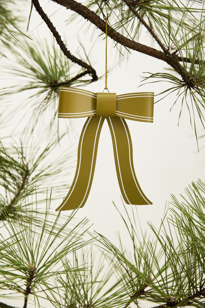 The Selah Bow Ornament 6x7.5" by Accent Decor adds festive charm to your Christmas tree, hanging elegantly from a pine branch with green needles against a plain light background.