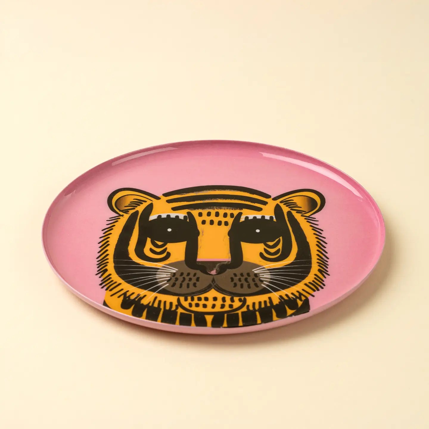The Indaba Pink Tiger Tray features a stylized black and yellow tiger face on a pink enameled surface, set against a light beige background—making it a bold accent decor piece for any space.