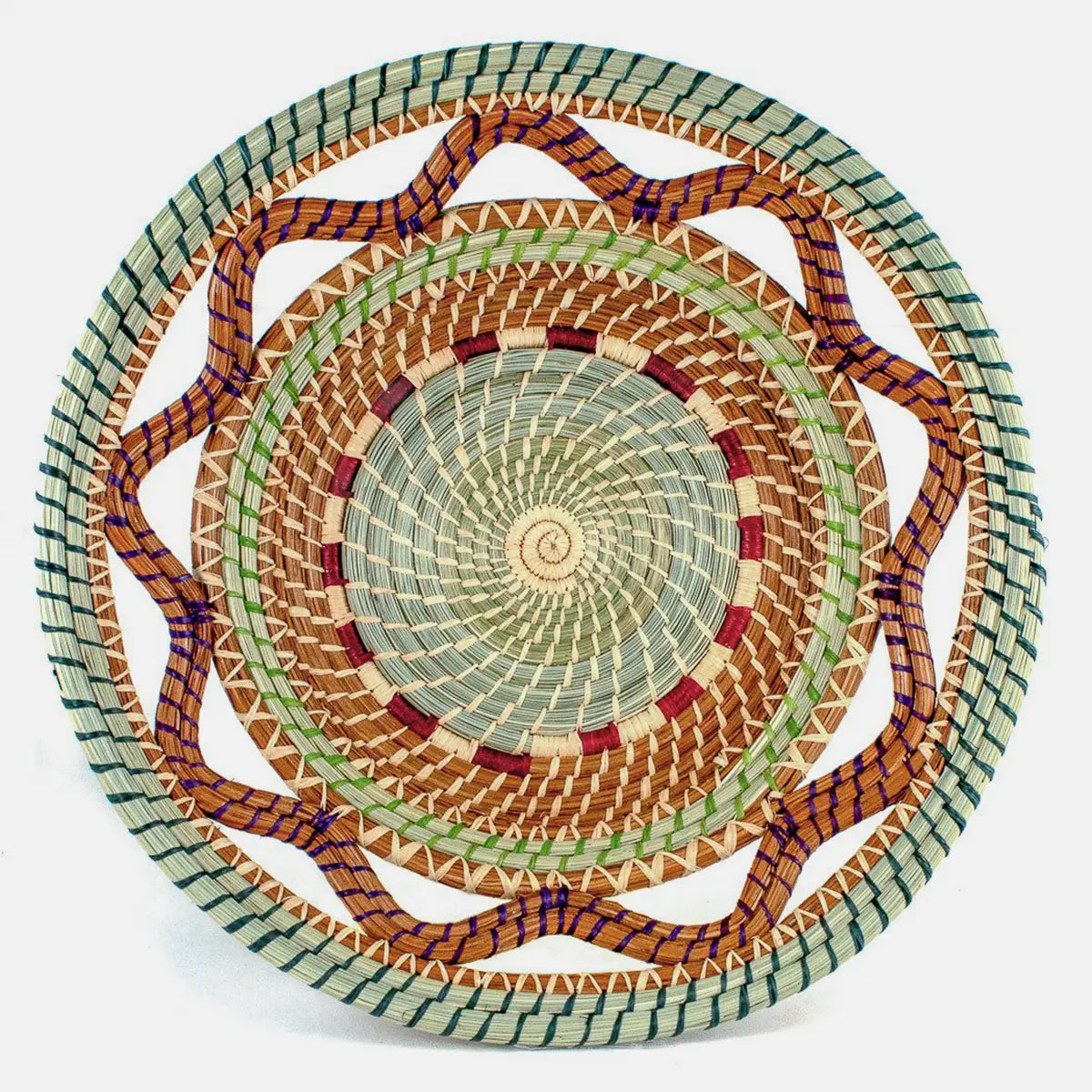 The Celestina Basket by Faire features a spiral center, wavy edge, and intricate green, brown, beige, red, and purple geometric patterns—showcasing the artistry of the Guatemalan Highlands.