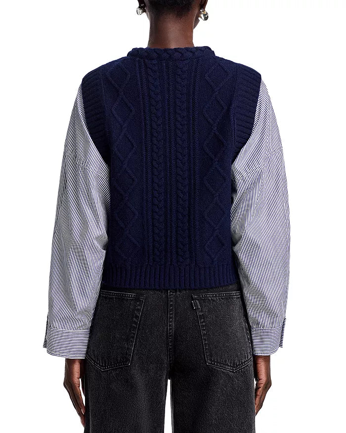 A person wearing the Caleb Cable Sweater from Sea New York over a button-front striped shirt and dark jeans is facing away from the camera, with the vest's diamond and cable pattern adding texture to the look.