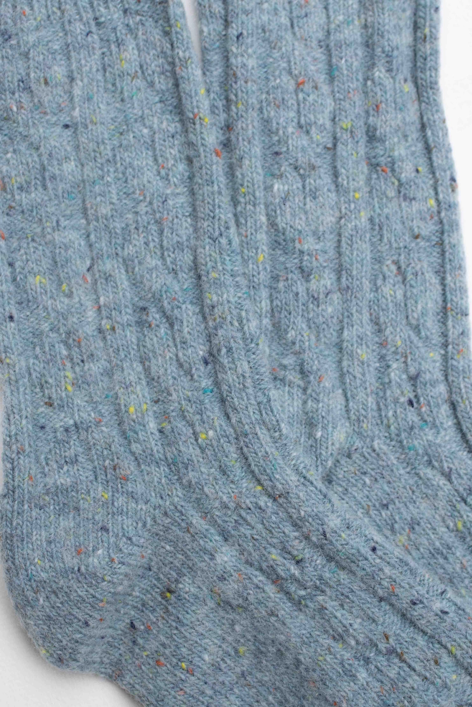 Close-up of Faire Wool Speckled Knit Socks in light blue, made from a wool-blend with a ribbed texture and multicolored specks throughout.